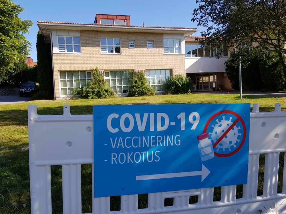 blå skylt med text om coronavaccin, gult tegelhus i bakgrunden
