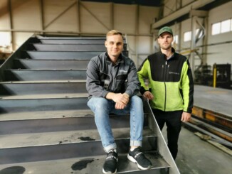 Två män som sitter och står vid ståltrappa.